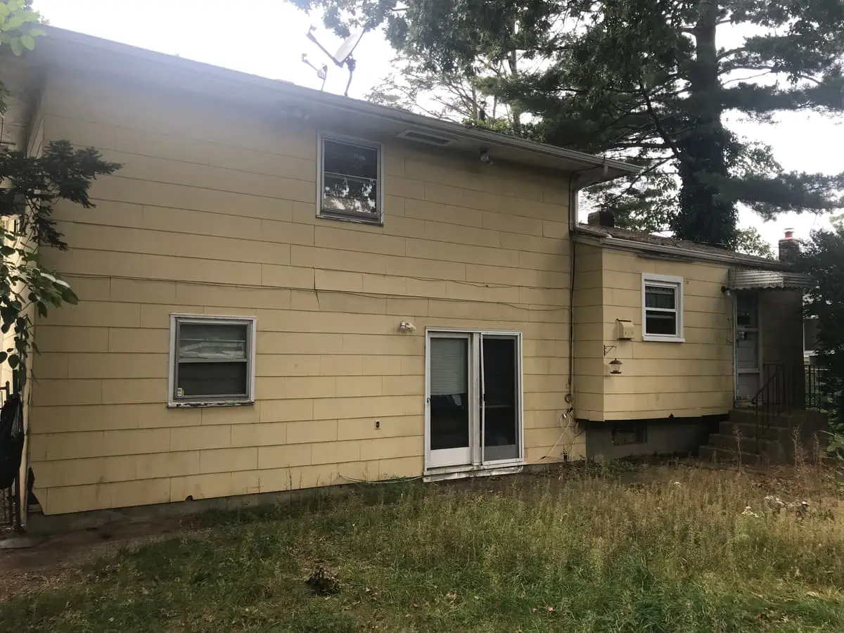 Selling a house with a failed cesspool in Westbury: back of a yellow shingled house with tall grass