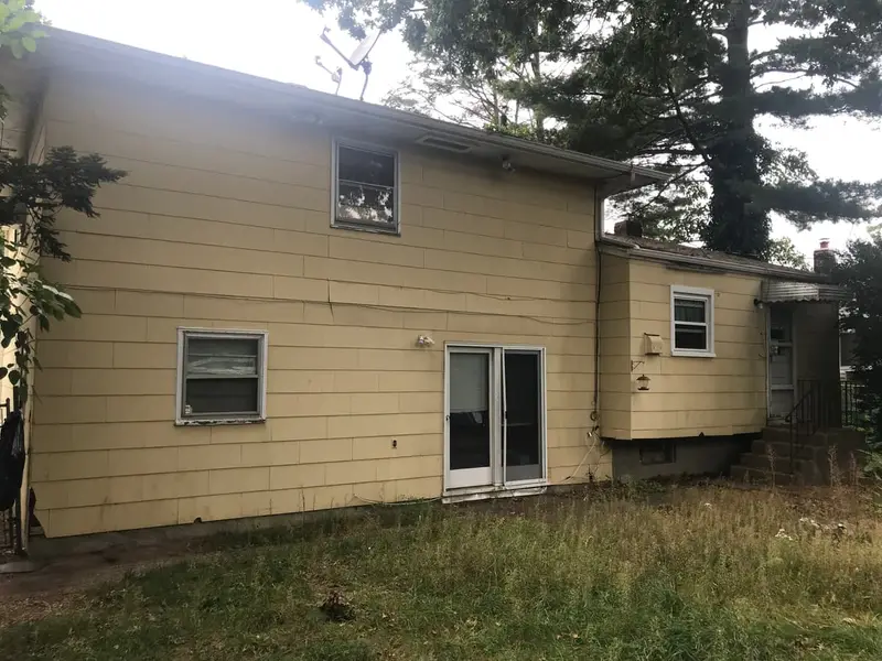 Back of a yellow shingled house with tall grass, Westbury, NY