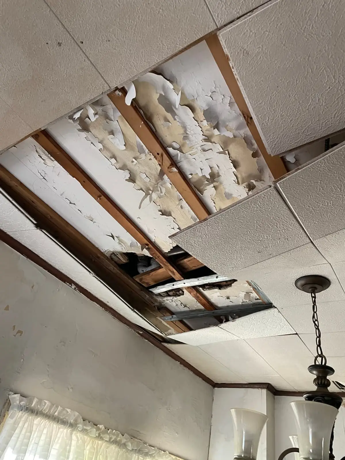 Selling a water-damaged house in Westbury: dropped ceiling tiles removed above a chandelier