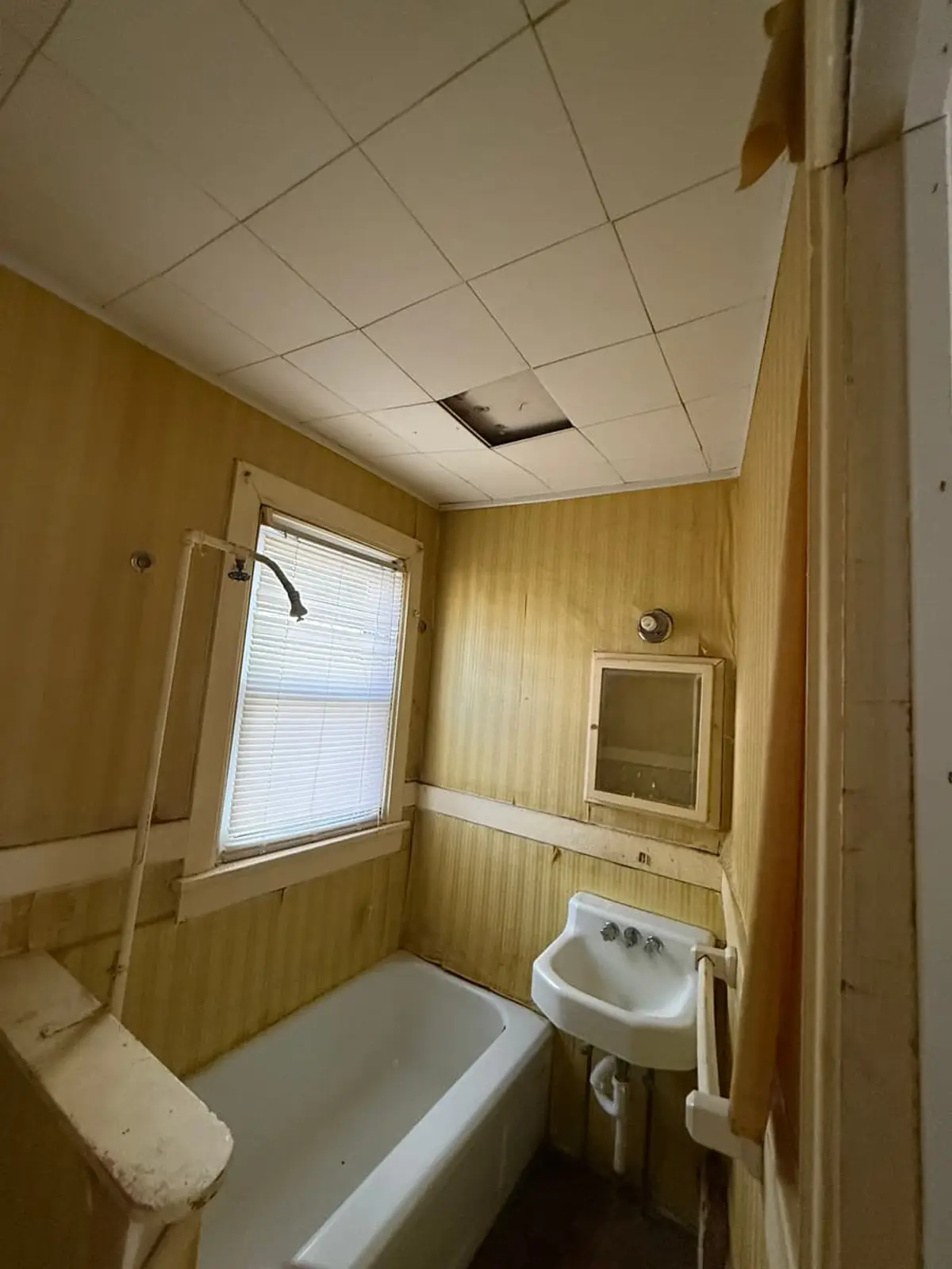 Selling a house near the LIRR in Westbury: narrow bathroom with yellowed wallpaper and a wall sink