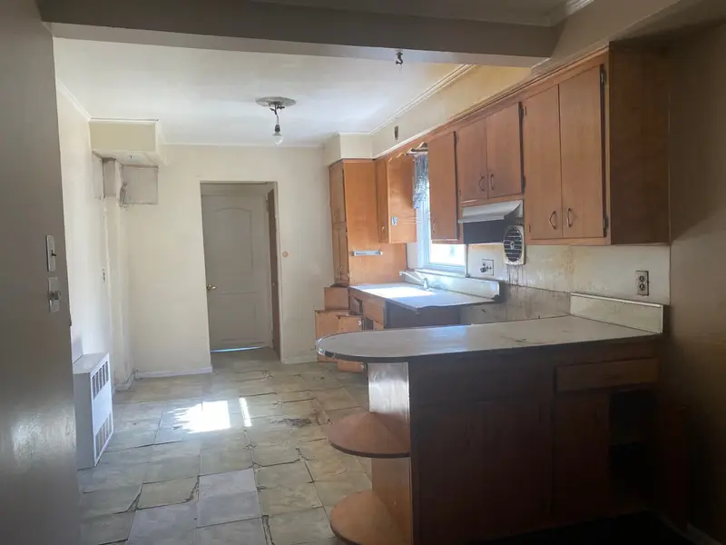 Vacant kitchen with wood cabinets and cracked floor tiles, Westbury, NY